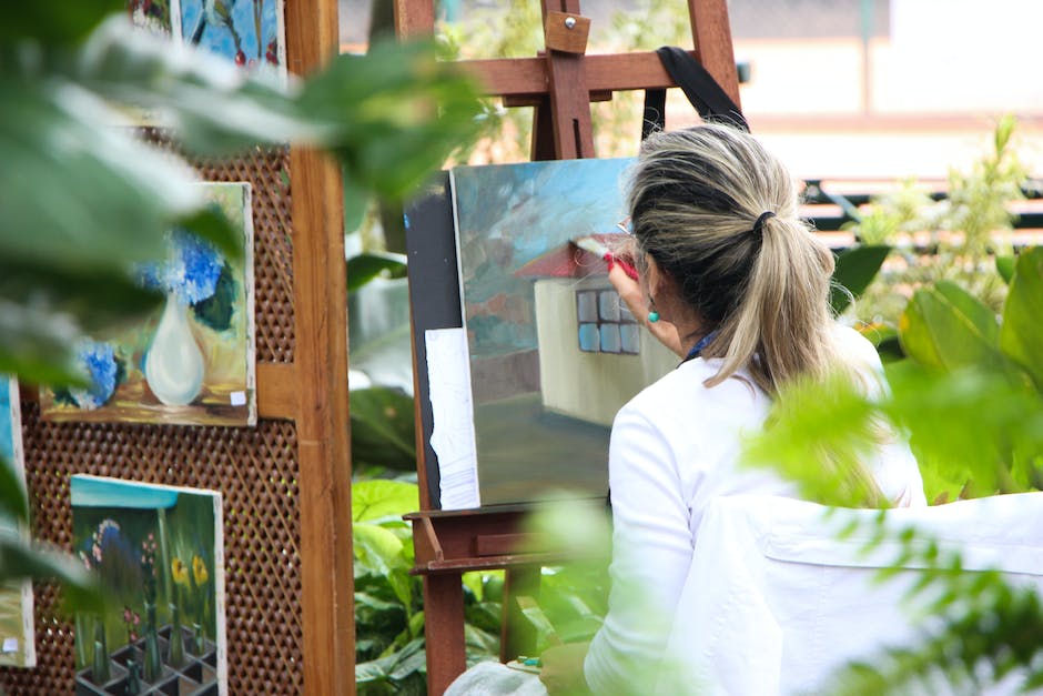 Image description: A person holding a paintbrush and painting a colorful garden with flowers and plants.
