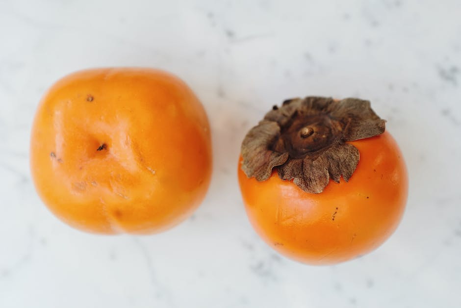 A close-up photo of ripe persimmons, showcasing their vibrant orange color and smooth skin texture.