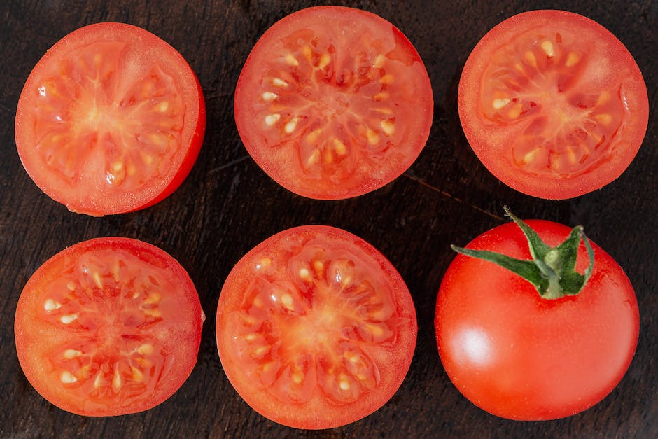 Image description: A close-up photo of tomato plants with healthy green leaves and ripe red tomatoes hanging from the vines.