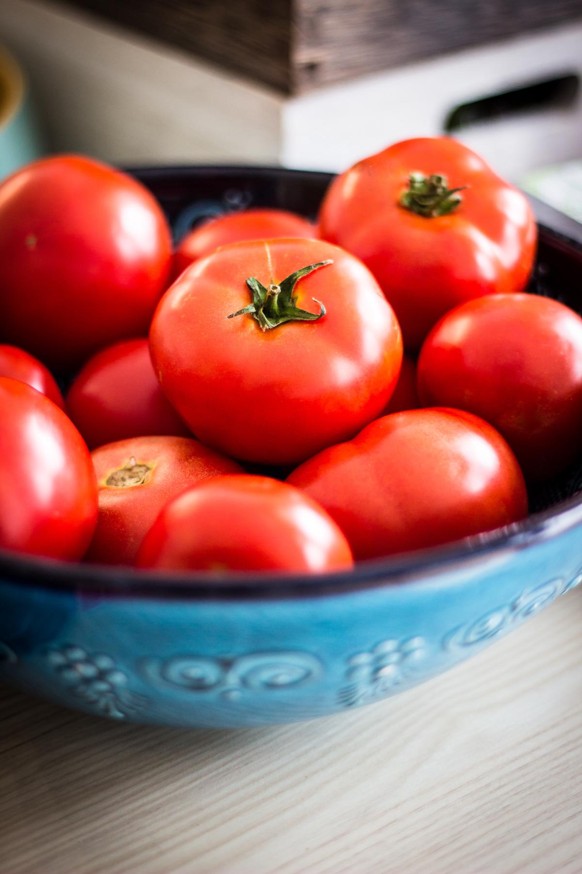 A bowl filled with tomato seeds surrounded by tomato slices and leaves.